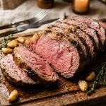 Sliced roast beef on a wooden board showing pink medium-rare centre with thyme and au jus