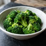 Steamed broccoli florets with sea salt in a white ceramic bowl on a dark slate surface