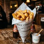 Thick cut British chips in a newspaper cone with malt vinegar and sea salt in a pub setting