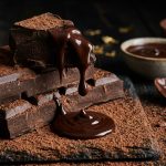 Dark chocolate pieces with melted chocolate dripping on cocoa dusted surface