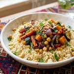 Bowl of fluffy Moroccan couscous with roasted vegetables, chickpeas and harissa on a colourful textile