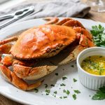 Whole steamed Dungeness crab on a white platter with melted butter, lemon and parsley