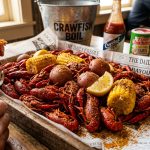 Pile of bright red boiled crawfish on newspaper with corn cobs, potatoes and lemon in a Cajun crawfish boil