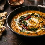 Bowl of rich red lentil dahl with mustard seeds and curry leaves served with naan bread