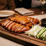 Crispy Peking duck sliced on a wooden board with spring onions, cucumber and hoisin sauce