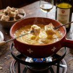 Traditional Swiss cheese fondue in a ceramic caquelon pot with fondue forks dipping bread cubes into bubbling melted cheese