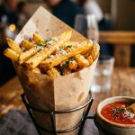 Golden crispy french fries in a paper cone with sea salt and ketchup dipping sauce