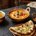 Indian takeaway spread with butter chicken, garlic naan, saffron rice and mango chutney in copper bowls