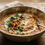 Steaming red lentil dal in a rustic ceramic bowl with crispy fried onion and fresh coriander