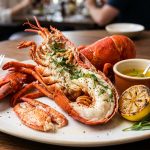 Whole steamed lobster split open on a white plate with clarified butter, lemon and tarragon