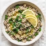 Bowl of fluffy quinoa with fresh herbs and lemon slices, overhead shot