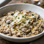 Creamy mushroom risotto in a white bowl with shaved parmesan and fresh thyme