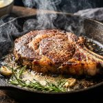 Thick ribeye steak searing in a cast iron skillet with rosemary and butter