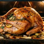 Golden roasted turkey with crispy skin in the oven surrounded by roasted vegetables and fresh herbs